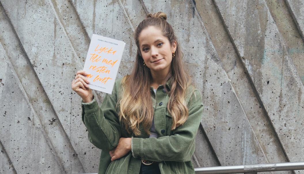 Isabel Boltenstern står upp och håller i sin bok, med en grå betongvägg bakom.