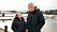 Janet och Lars står vid en hamn. De har på sig svarta jackor.