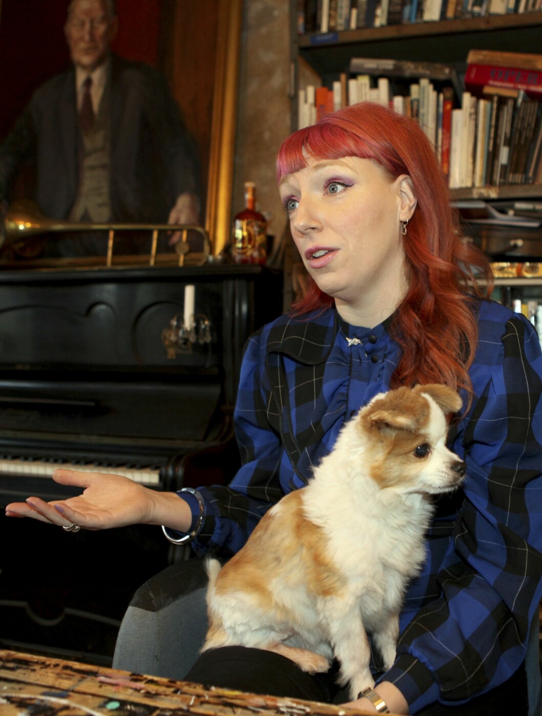 Josefin Johansson i en rustik miljö med böcker i bakgrunden, och med den lilla hunden Woody i knät.