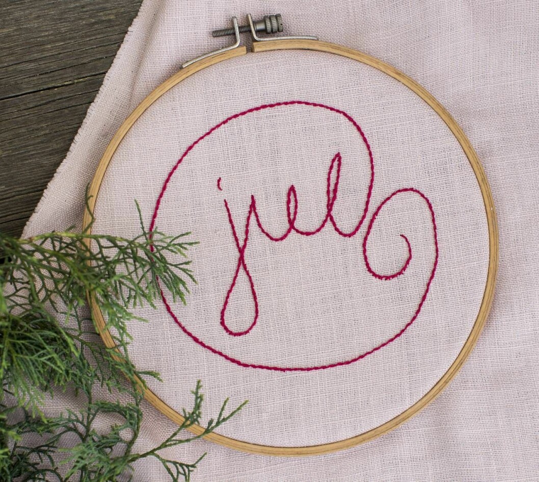Tavla med broderad text som säger "jul"