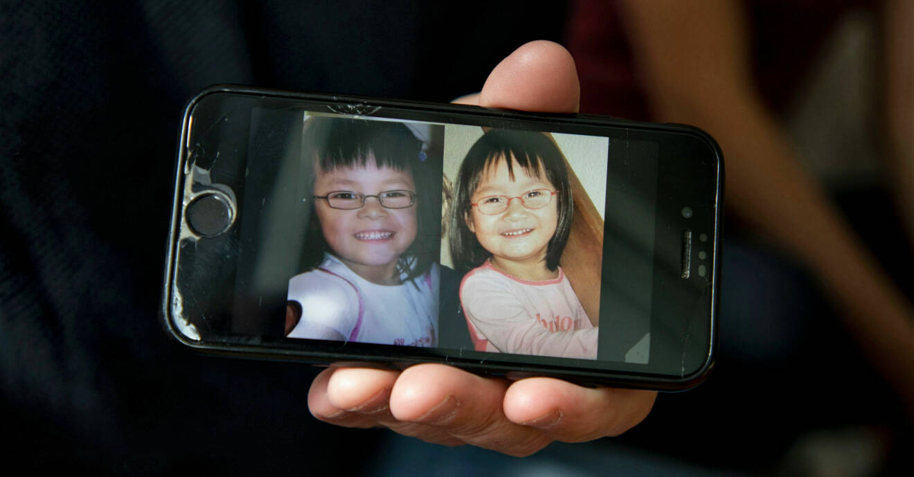 En hand håller upp en mobil med foton på systrarna när de var små. De är väldigt lika och bär båda glasögon.