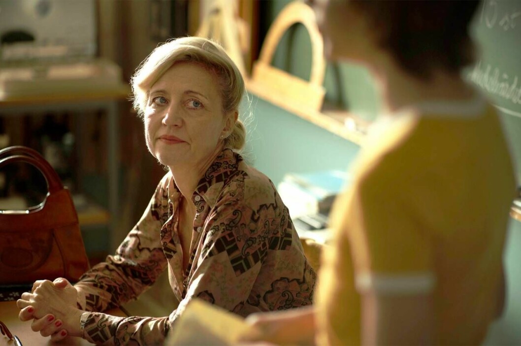 Klara Zimmergren spelar skolfröken i biofilmen som gjorts efter Jonas Gardells roman, <em>En komikers uppväxt</em>. Foto: Pressbild Skådespelaren Klara Zimmergren som lärare vid en kateder i filmen En komikers uppväxt.