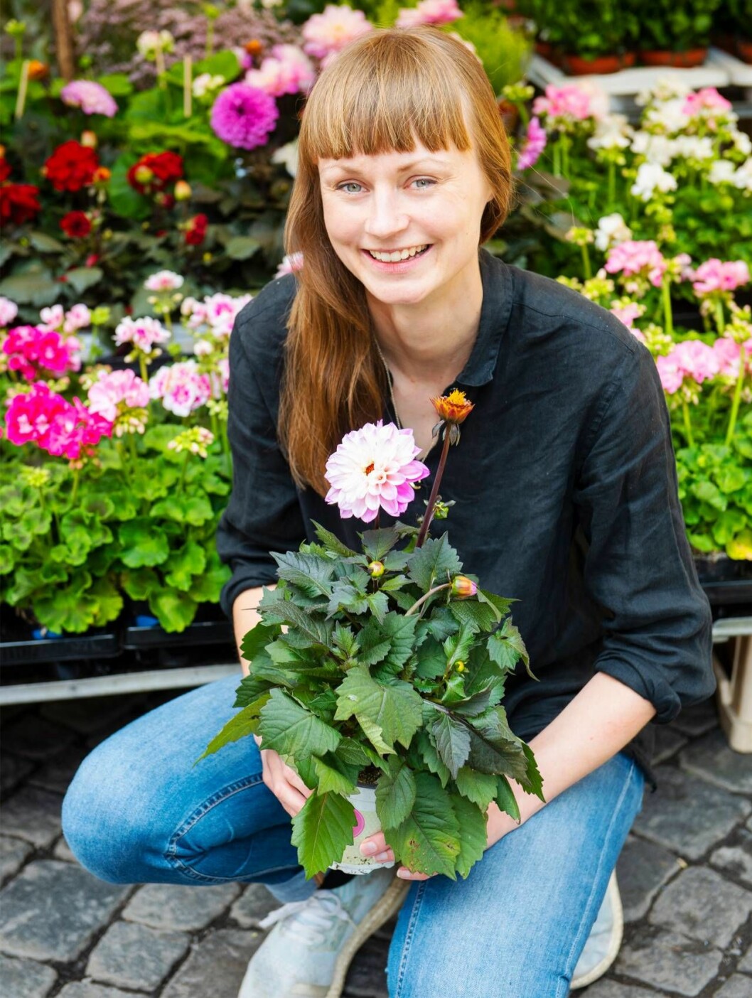 En ung kvinna, Johanna Nilsson, sitter på huk med en blomma i famnen.