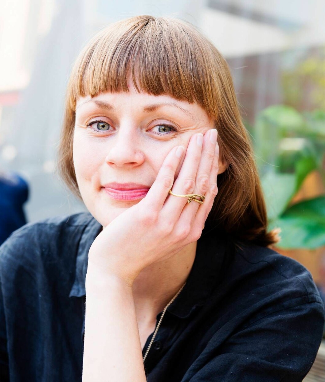 Mode är fortfarande ett av Johannas största intressen men hon prioriterar färre och finare plagg med hållbar produktion och minimal negativ miljöpåverkan. Foto: Theresia Khölin En ung kvinna med lugg sitter med huvudet i handen.