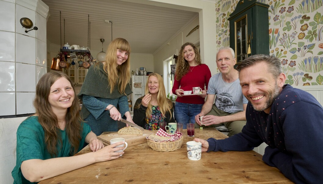 Sex av kollektivboendets medlemmar tar en gemensam fika i köket där de ibland lagar mat ihop men oftast lagar de mat var för sig.
