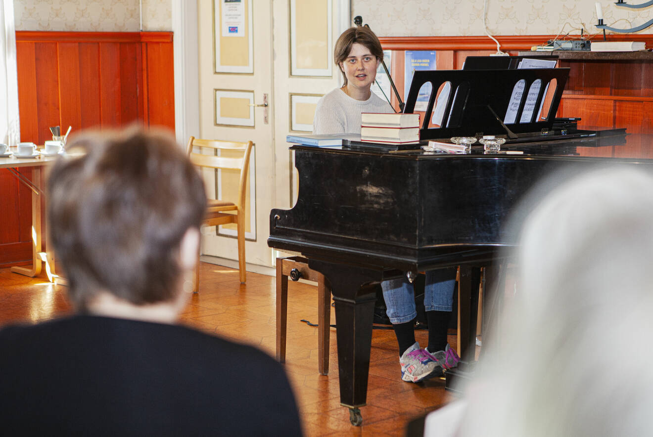 Körledare och undersköterska Matilda Norlöv sitter vid ett piano framför kören