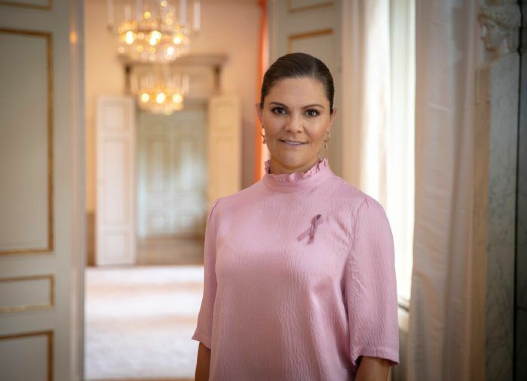 Kronprinsessan Victoria visar upp Rosa bandet 2020, iförd en rosa topp från Rodebjer. Kronprinsessan Victoria med rosa bandet 2020.