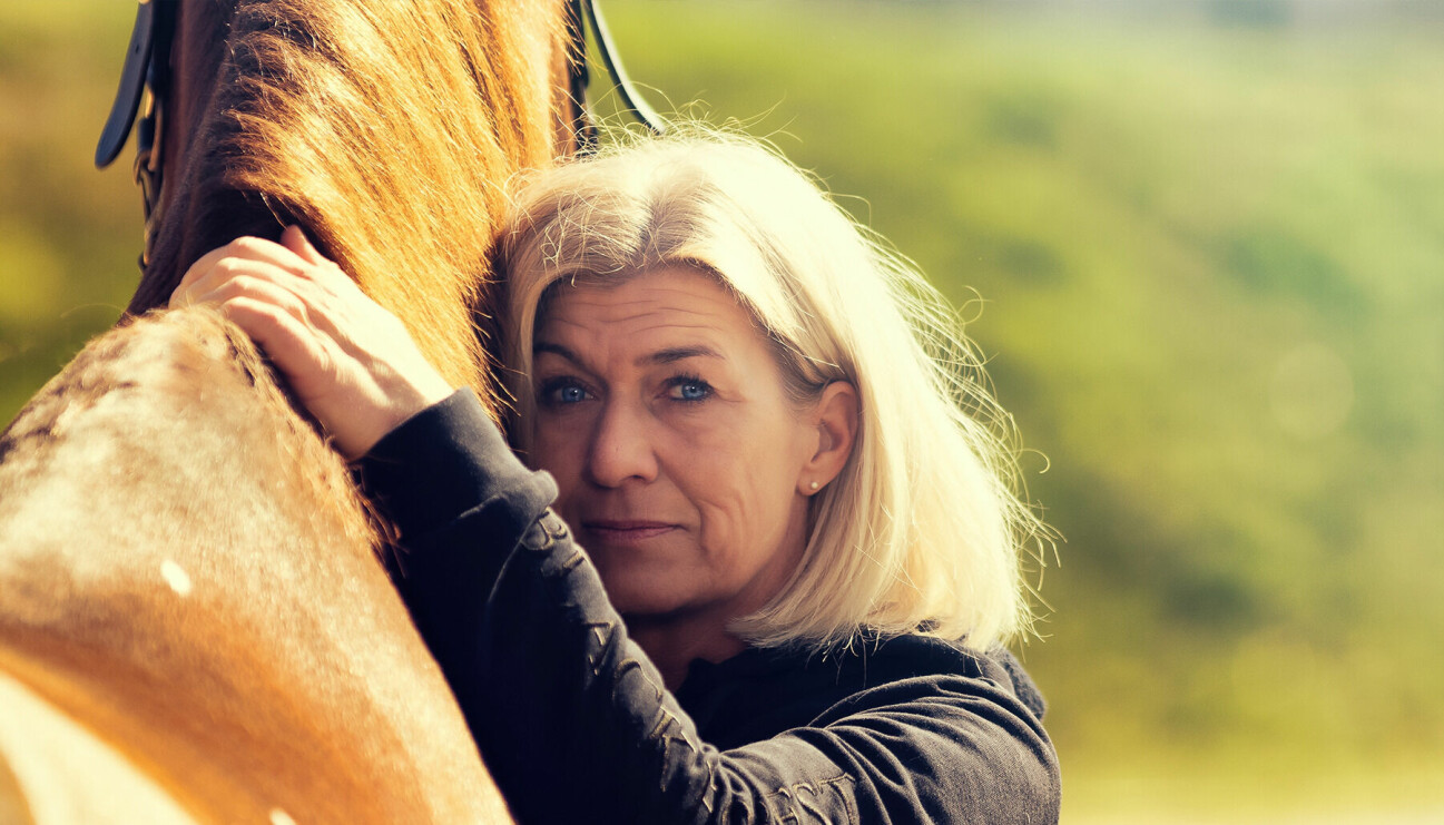 En kvinna i medelåldern håller om en häst.