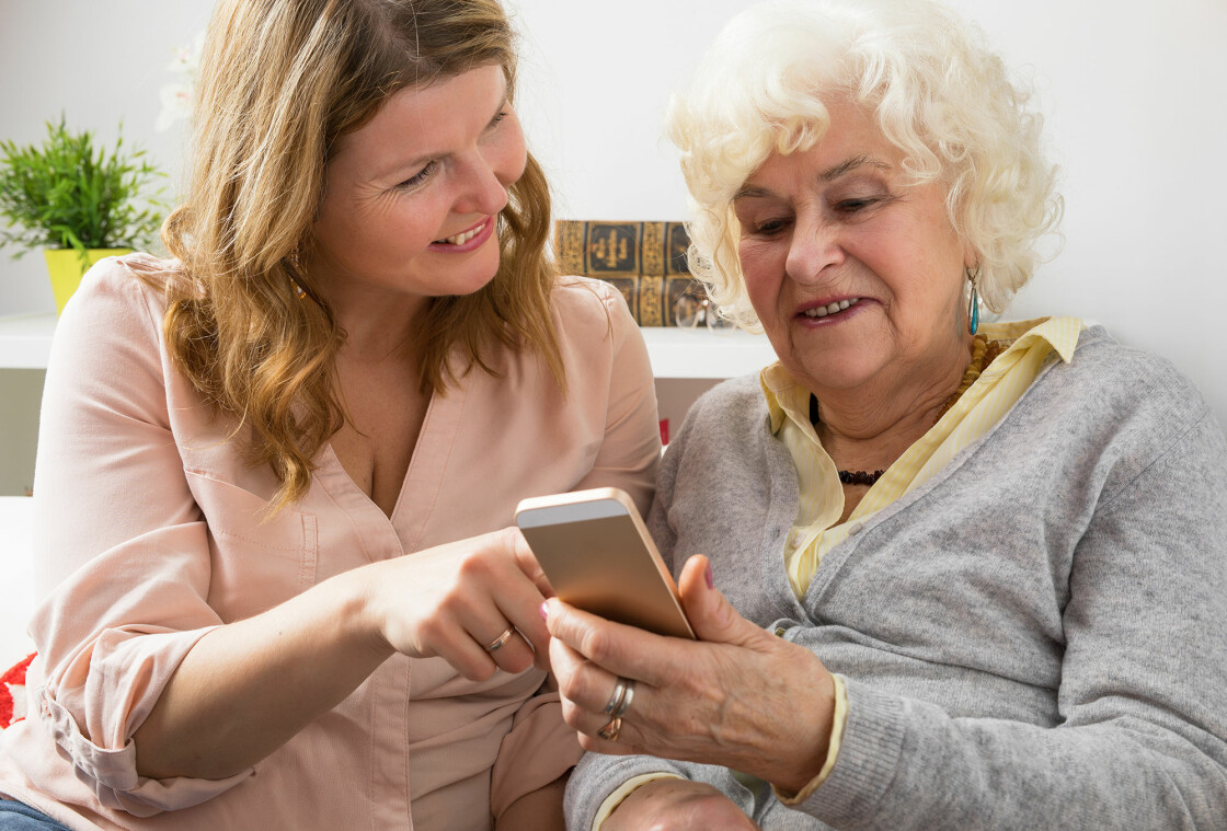 Kvinna hjälper äldre kvinna att hantera sin telefon.