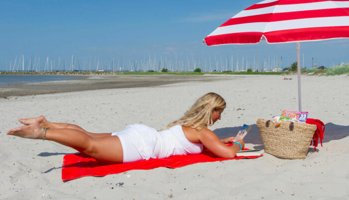 Kvinna ligger på mage på strandhandduk och tränar genom att lyfta benen högt.