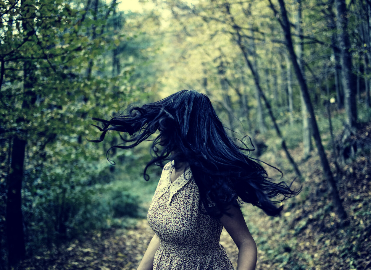 Kvinna med mörkt hår jagas i en skog.