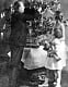 Kvinna och flicka med docka ser på när far klär granen med mycket glitter. 1929.