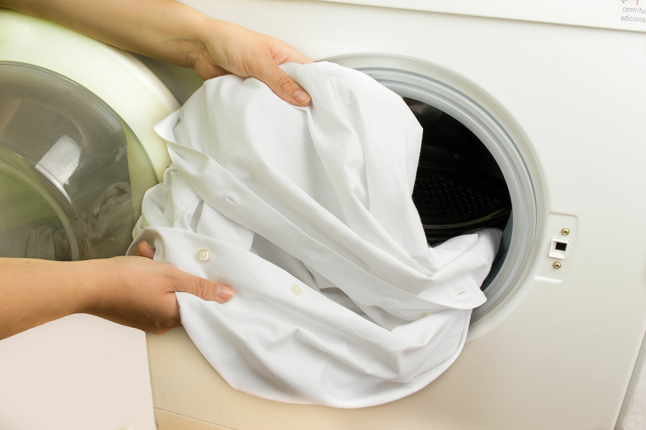 Kvinna plockar ut ett vitt plagg ur tvättmaskinen.