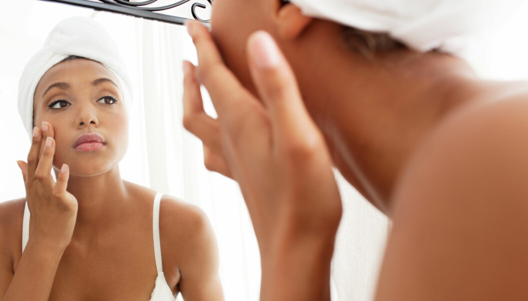 Kvinna rengör sitt ansikte framför spegeln.