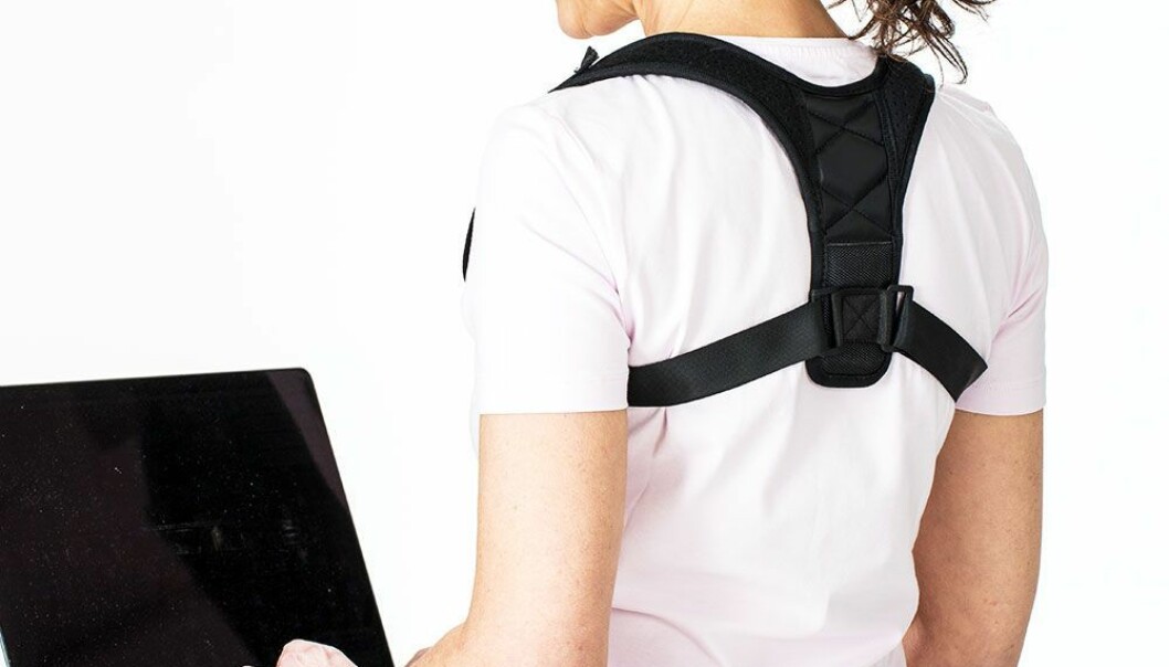 Kvinna sitter vid en dator i klädd hållningsvästen som minskar ryggsmärta och stärker hållningen,