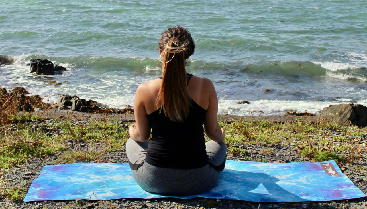 Kvinna sitter vid havet och tränar yoga.