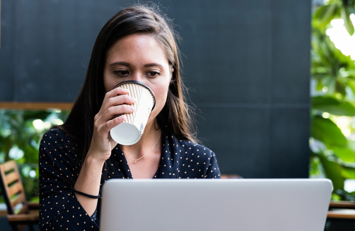 Kvinna sitter vid sin dator och dricker kaffe.