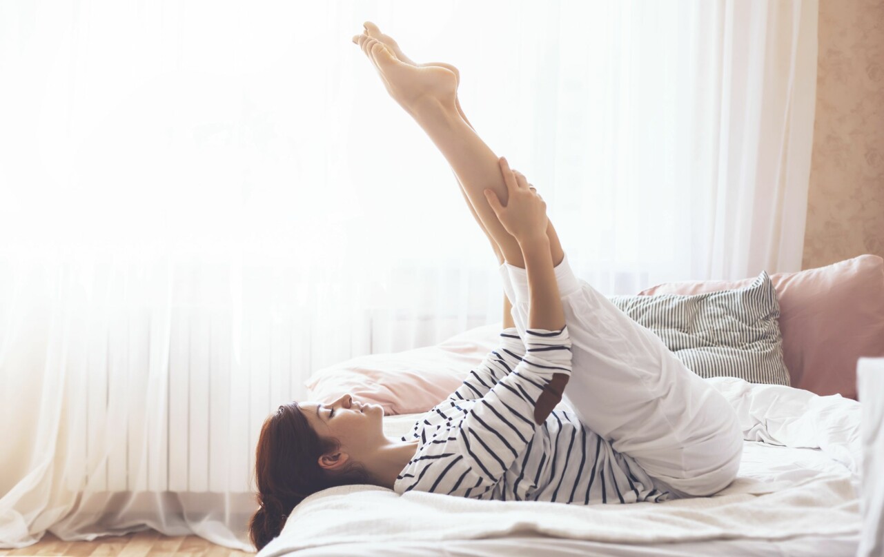 Kvinna som stretchar benen i sängen