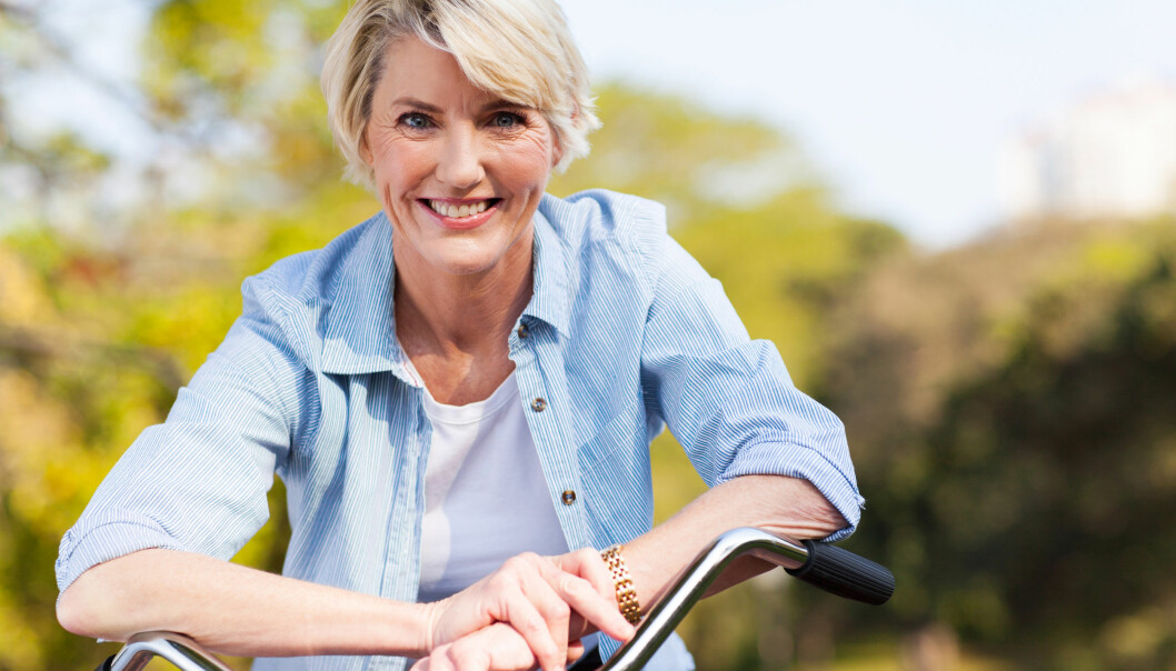 Mogen kvinna lutar sig över cykelstyret med ett leende.