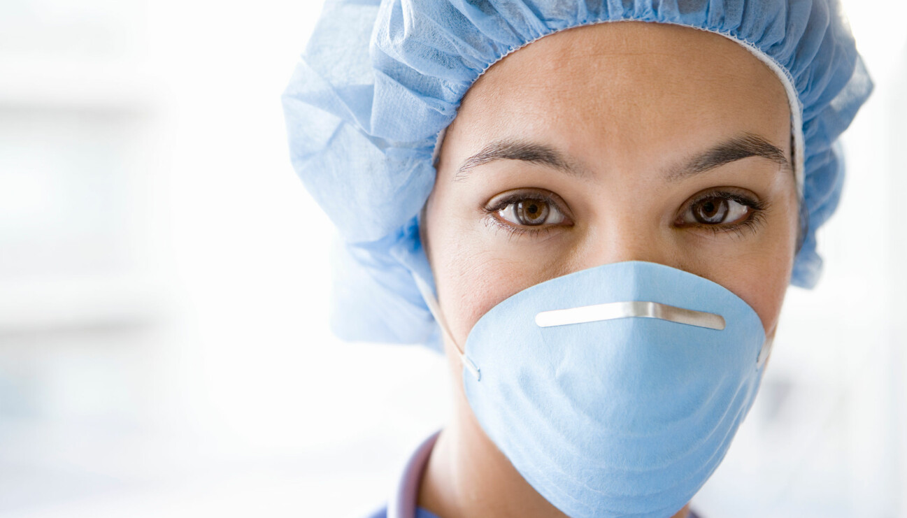 Kvinnlig sjuksköterska med mask och hårnät som säkerligen tjänar sämre än män i jämförbara yrken.