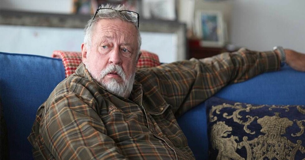 Leif har alltid haft kvar sin barnatro, vilket kan ha en koppling till hans intresse för mysterier. – Kanske är jag troende för att det handlar om livets största gåta. Foto: Frida Funemyr Leif GW Persson i en blå soffa.