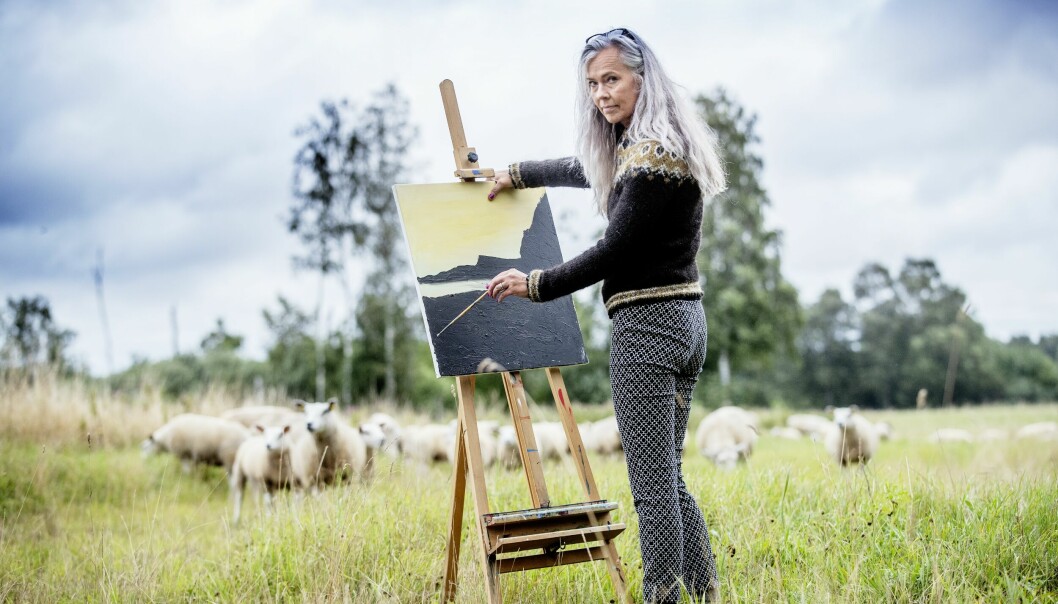 Lene Søe Rasmussen står vid sitt staffli framför en äng med får och berättar om hur det var när hon sålde de mesta av sina ägodelar, sa upp lägenheten och flyttade i sin en husvagn.