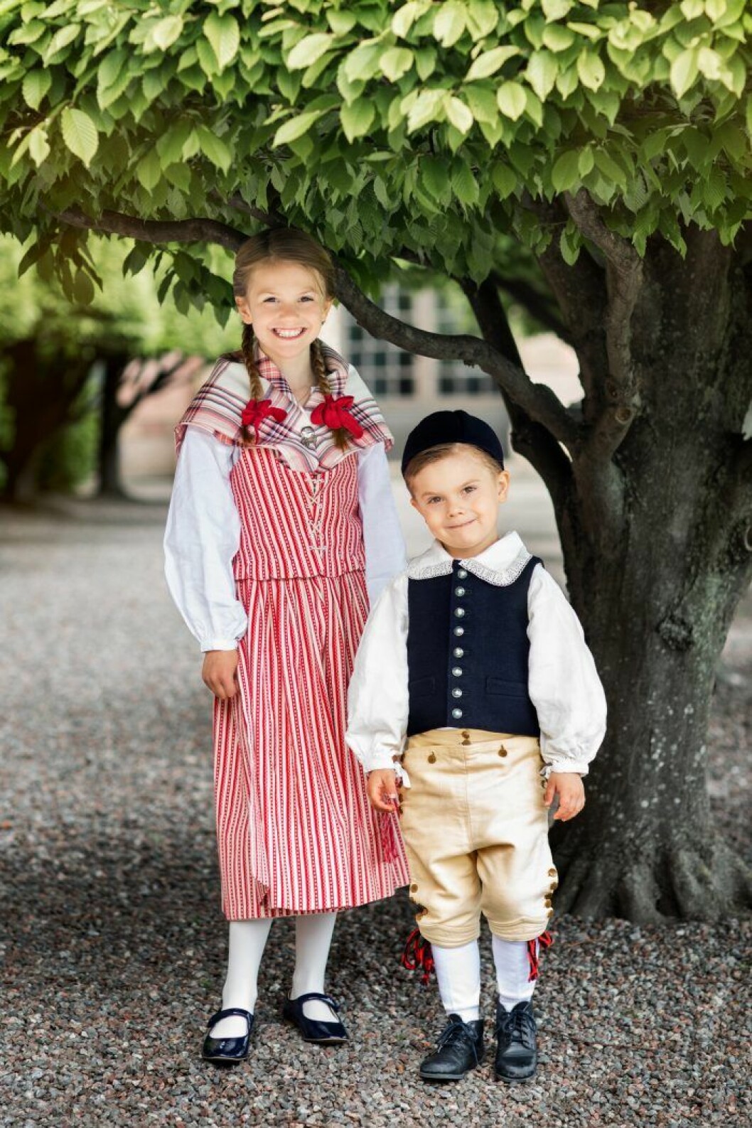 Estelle är polkagrisrandig och fin, och har röda rosetter i flätorna. Och samma röda rosetter går igen i lillebror Oscars knätofsar. Prinsessan Estelle i sin nya folkdräkt från Skedevi. Prins Oscars dräkt är från Ingelstad i Skåne.