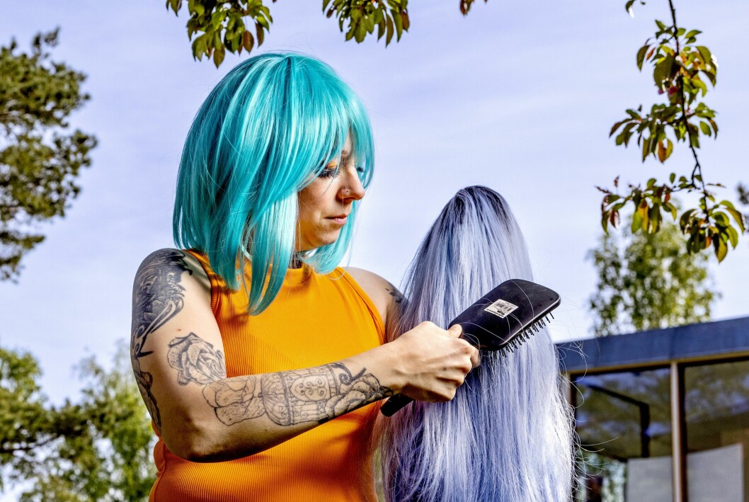 Helst använder Lena peruker som är tillverkade av äkta hår. De håller bättre och går både att färga, klippa och göra frisyrer med. Lena, i orange topp, bär en illande turkos peruk med axellångt hår. I händerna har hon en annan långhårig peruk, i en blålila ton, som hon är i färd med att borsta.
