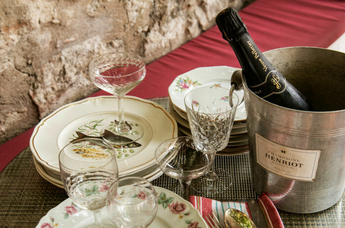 Sophia besöker samma utomhusloppis varje torsdag och lördag i jakt på vinglas eller något annat användbart. Loppisfyndade tallrikar och glas samt en champagnehink med en flaska i.