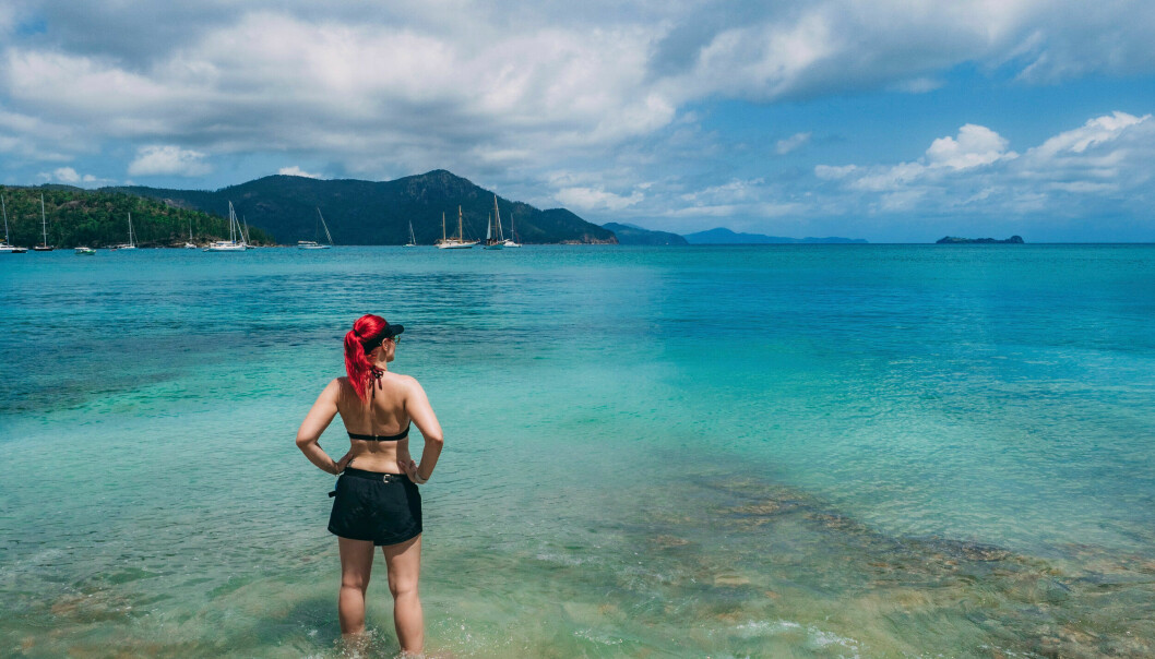 Louise står i vatten på en strand i Peru. I bakgrunden syns hav och berg. Hon har håret uppsatt i en hästsvans och har på sig shorts och bikinitopp.