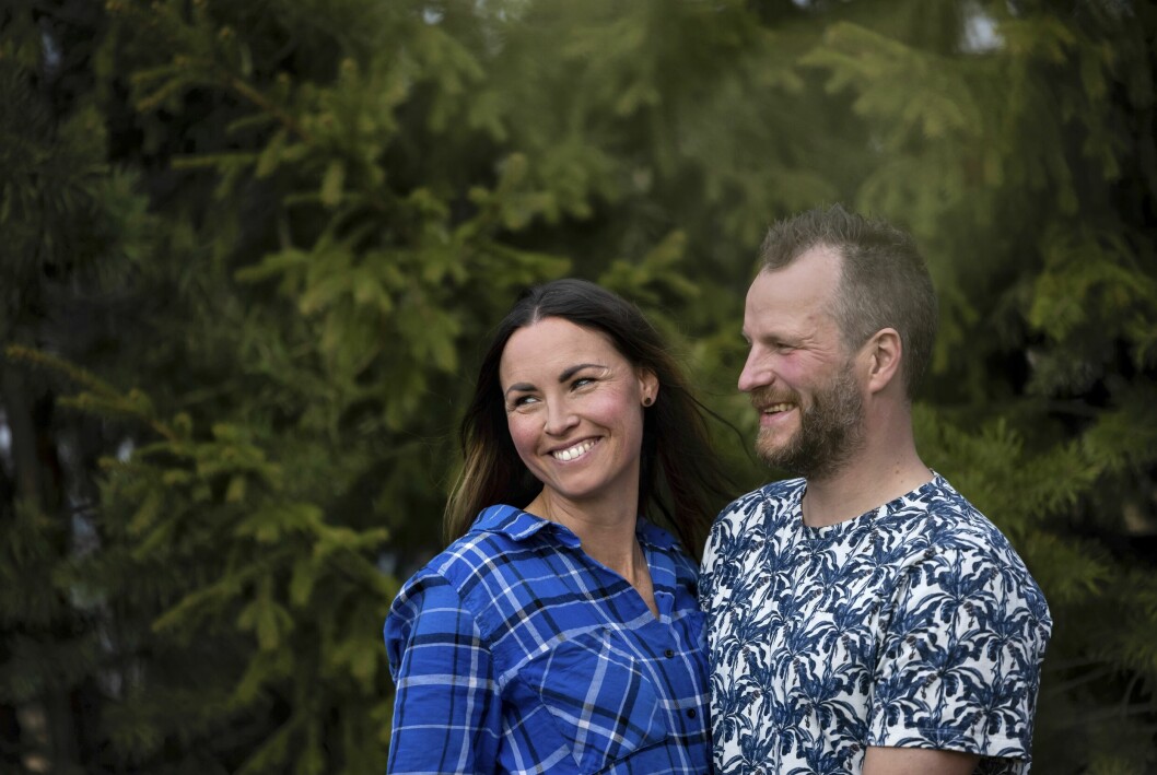 Malin och André håller om varandra och skrattar, där de står utomhus med barrträd i bakgrunden.