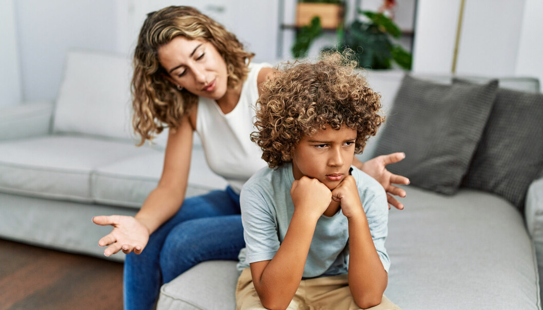 Kvinna i 40-årsåldern sitter i en soffa bakom sin son i 10-årsåldern som ser sur ut.