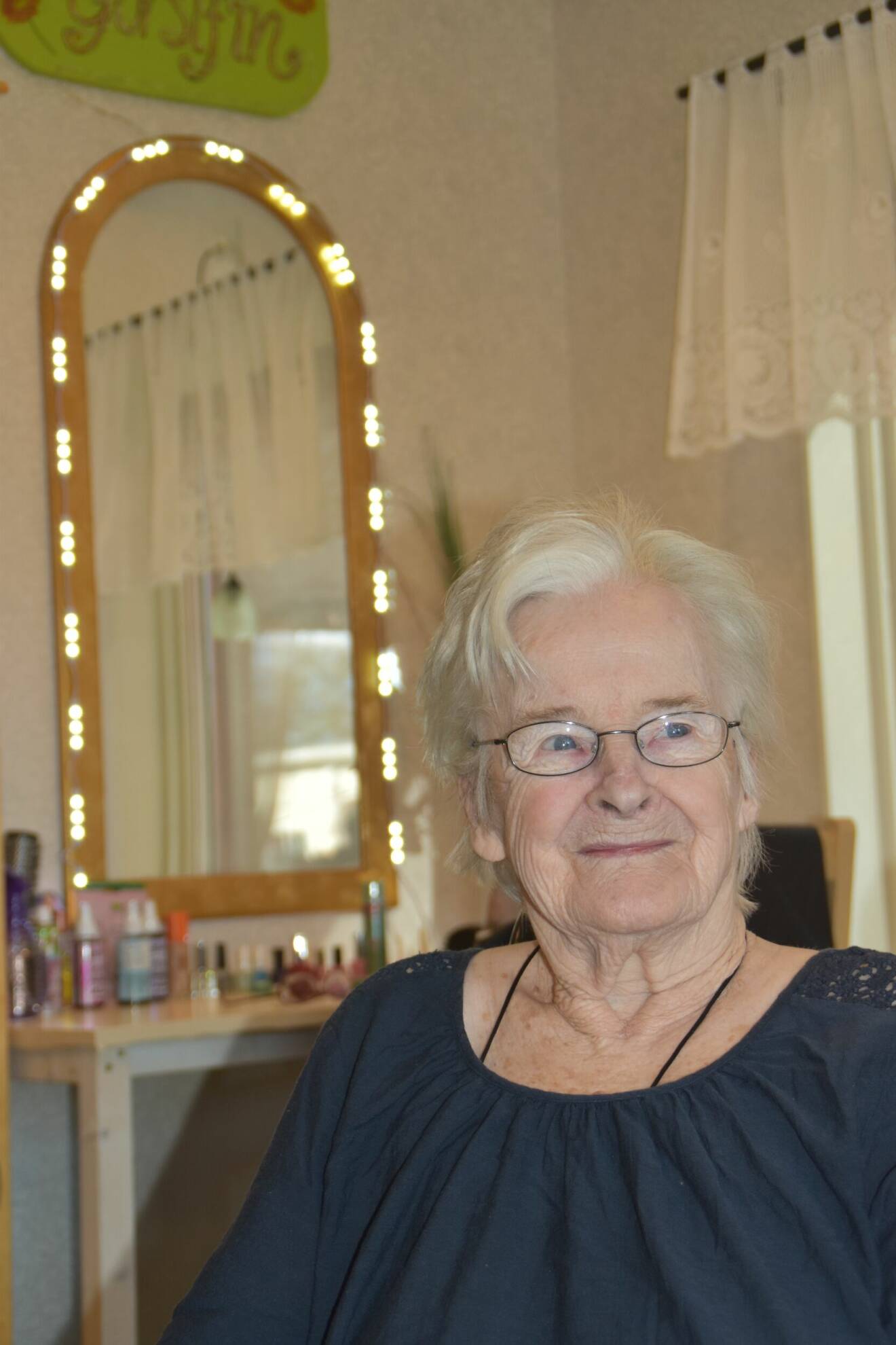 En kvinna på äldreboendet tittar nöjt in i kameran efter att ha fått både sig hår lagt och sina naglar målade.