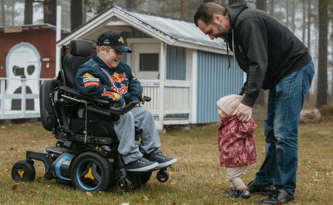 Marcus har en nära relation till sin syster Emelie, och älskar att busa med systerdottern Elly som här får en hjälpande hand av sin morfar Jörgen. Marcus Aftelöv sitter i sin rullstol och ler mot systerdottern Elly som får hjälp att stå av sin morfar Jörgen Aftelöv.