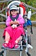 En liten flicka sitter i en sittvagn med en rosa filt över knäna.