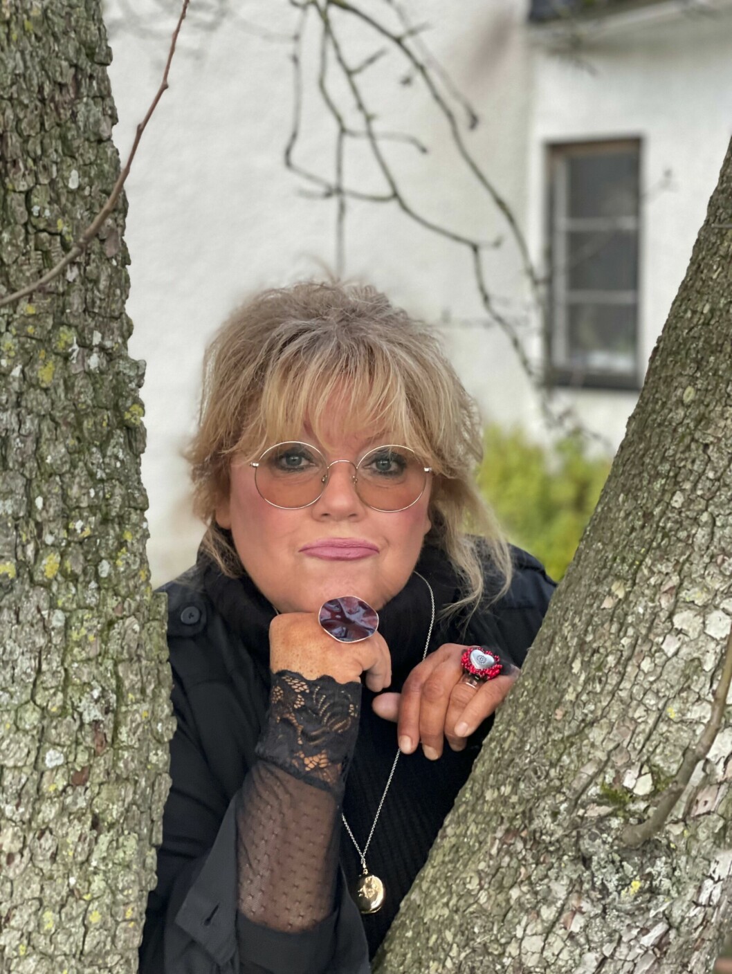 Marie har beskrivit sig själv som the f***ing queen of glesbygd, sorg och psykisk ohälsa, – en slags omskrivning av The queen of f***ing everything som är titeln på Jonas Gardells show. Marie, klädd i svart och med stora ringar på fingrarna, kikar fram mellan två trästammar.