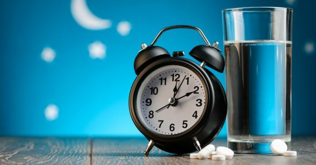 En väckarklocka, sömnpiller och ett glas vatten på nattduksbord