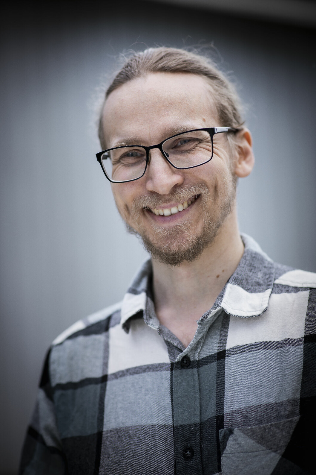 En man i 40-årsåldern i rutig skjorta och glasögon, ler stort och ser in i kameran.