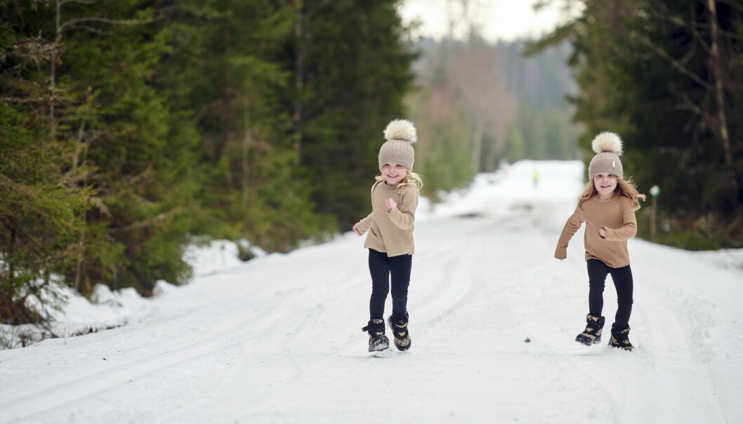 Nomie och Minelle springer tillsammans i full fart på en snöig väg med granar på vardera sidan av vägen