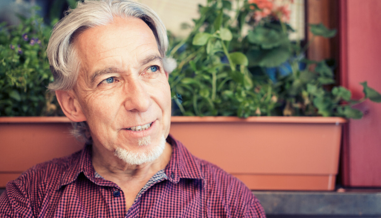Leende man i 60-årsåldern, med tjockt grått hår i mittbena och klarblå ögon, sitter framför en blomlåda.