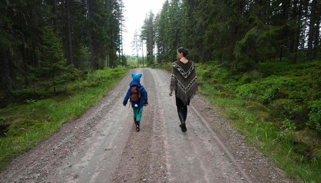 Skogspromenad i gemenskap. Mor och barn på promenad på en liten skogsväg.