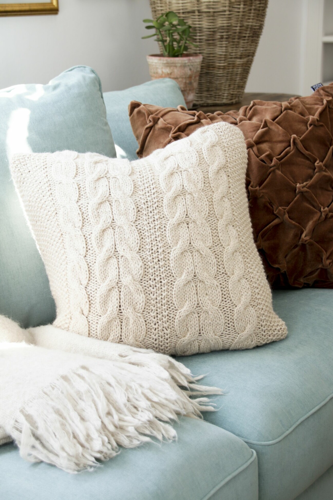 En stickad kudde i en turkos soffa.