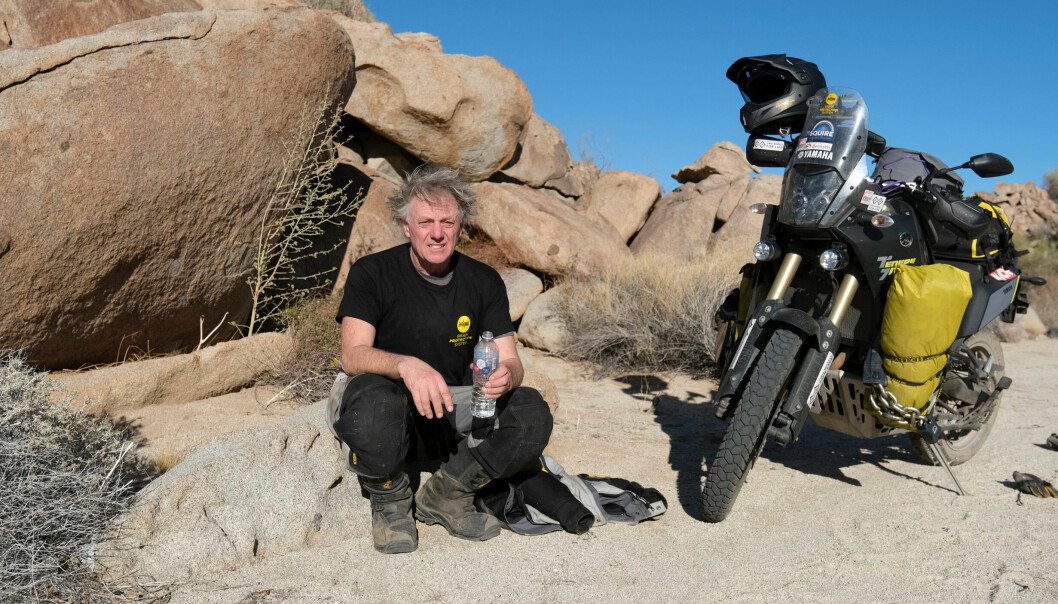 Nick Sanders sitter på en sten bredvid sin svarta motorcykel, i öknen i Mexiko.