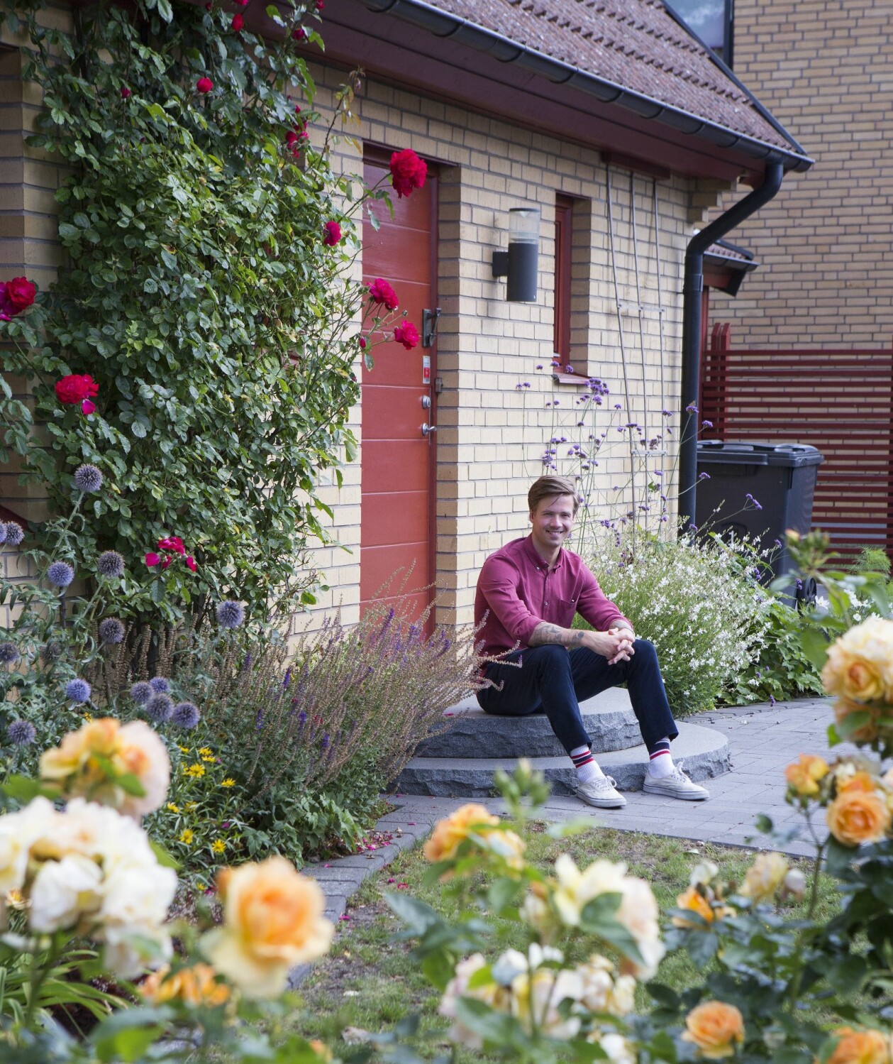 Nils mitt i blomsterprakten på trappan till barndomshemmet på Skolgatan i Anderslöv. Nils på trappan till barndomshemmet i Anderslöv omgiven av en blomstrande trädgård