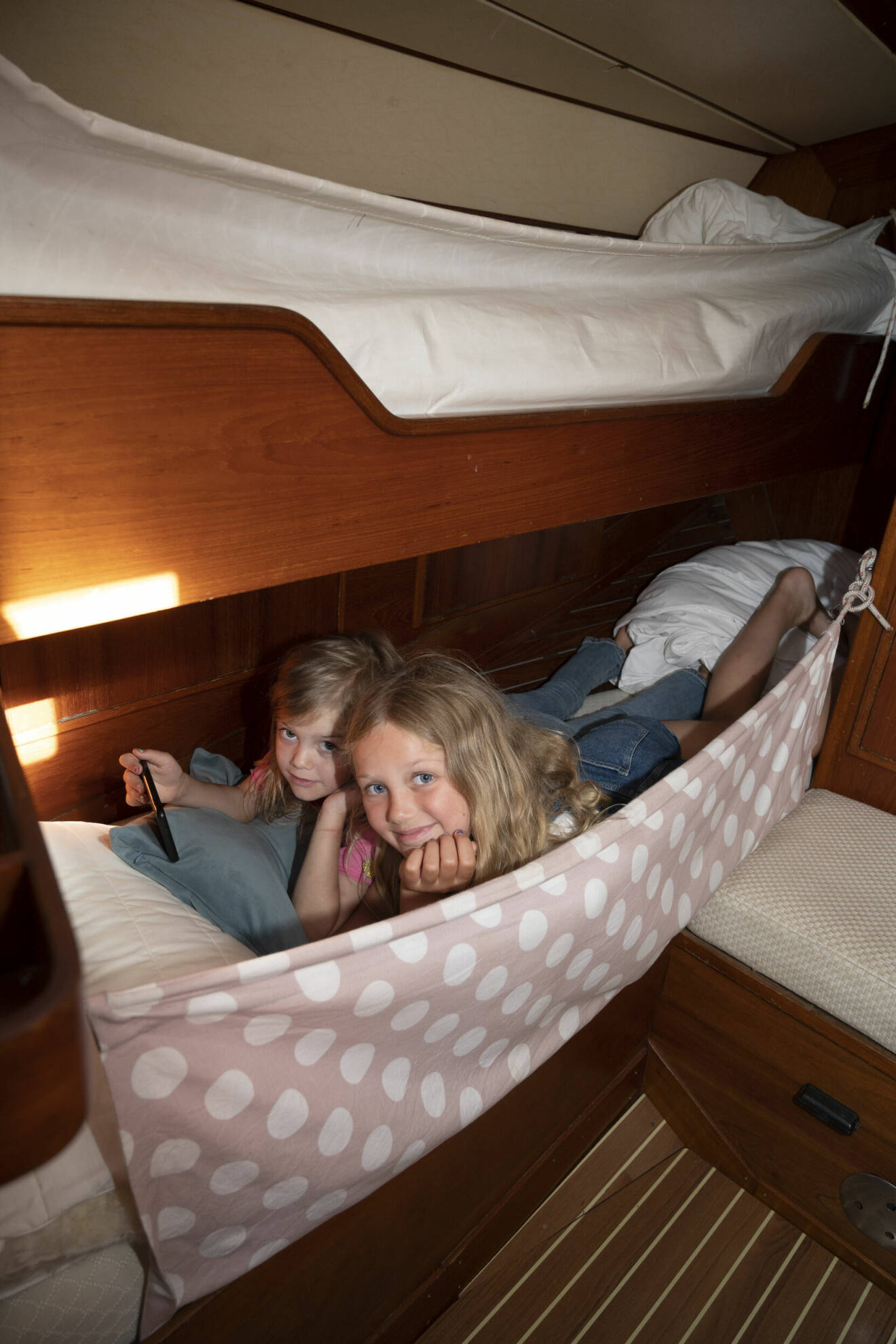 Nora-Li och Juni ligger i en säng och tittar in i kameran. Sängen är smal och på båten.