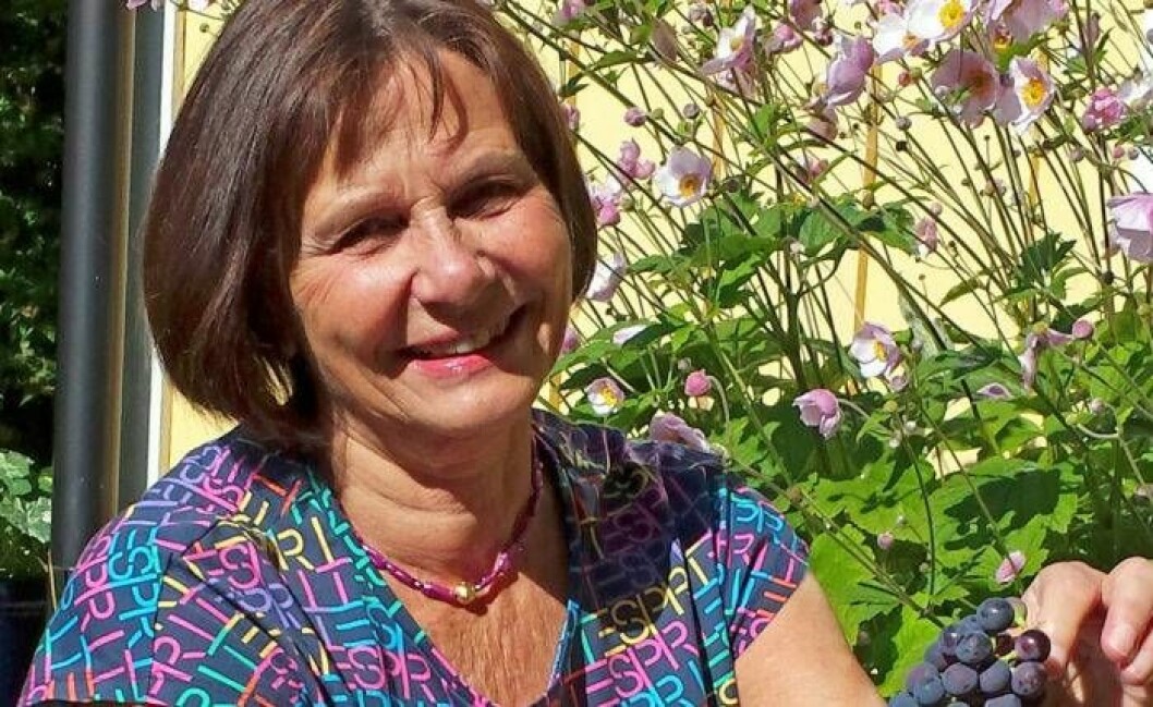 Yvonne Alin Jansson i trädgården mot gul husvägg.