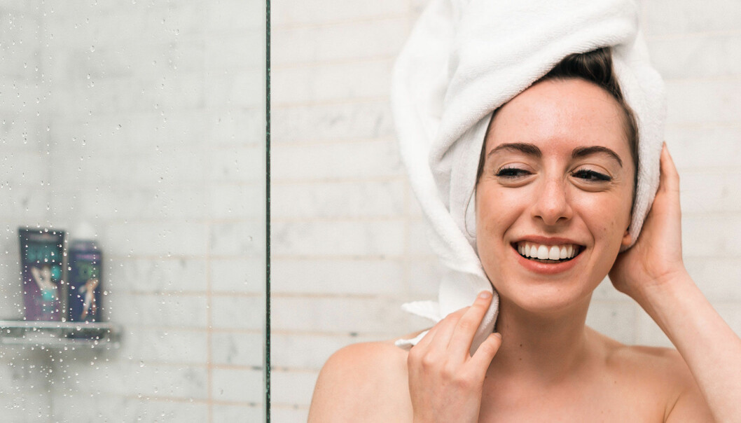 En kvinna som ler i duschen med en handduk på huvudet.