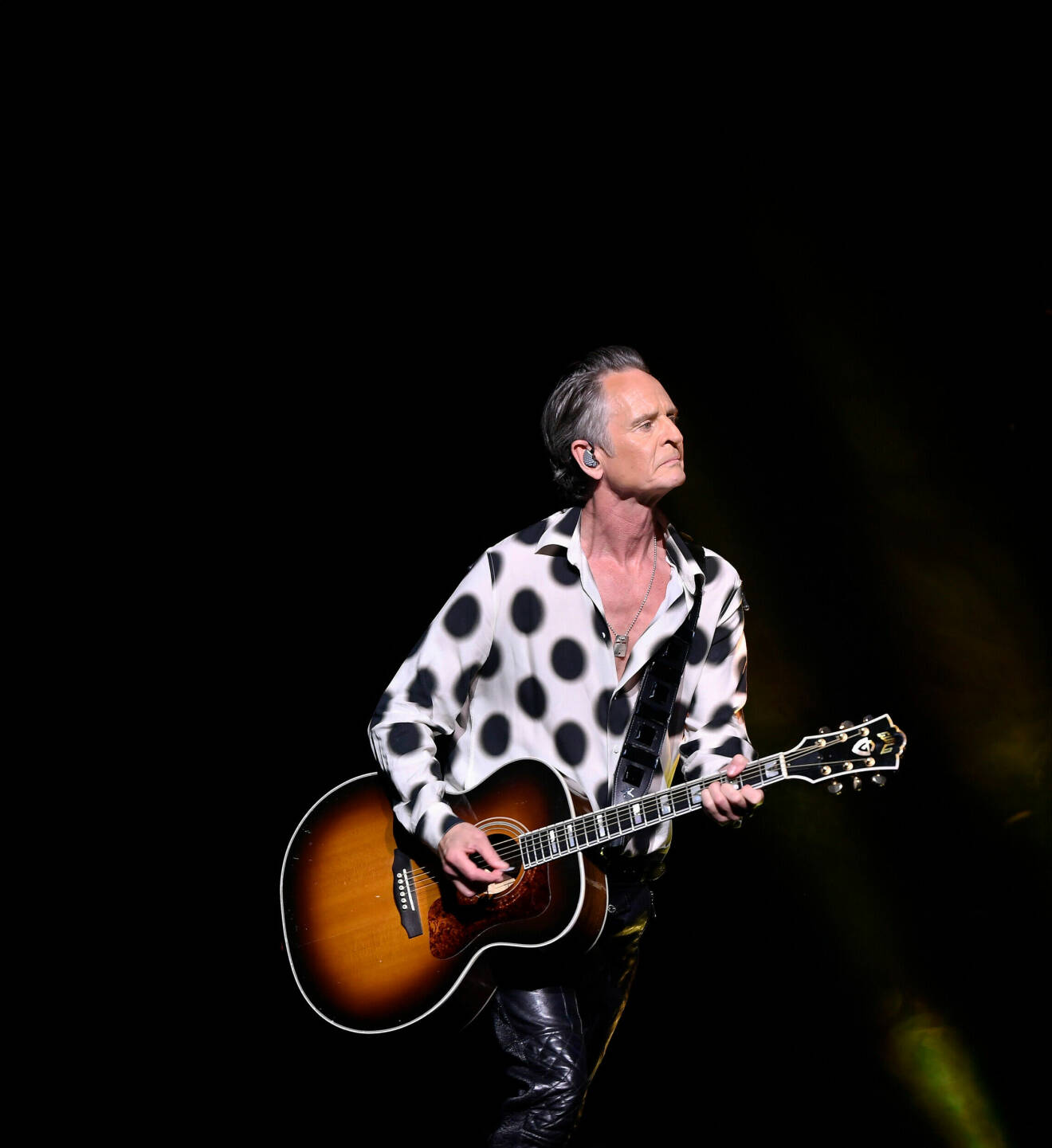 Artist på scen i prickig skjorta med gitarr.