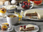 På ett frukostbord med bär, ägg, uppskivad grepefrukt, te och kaffe står ett fat och en tallrik med tårta.