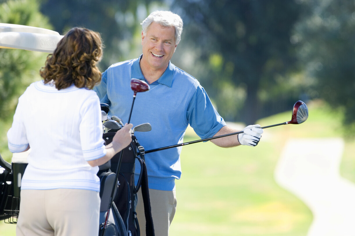 En man i 50-årsåldern ler mot en kvinna som står med ryggen mot kameran. De befinner sig på golfbanan och båda har golfklubbor i händerna.